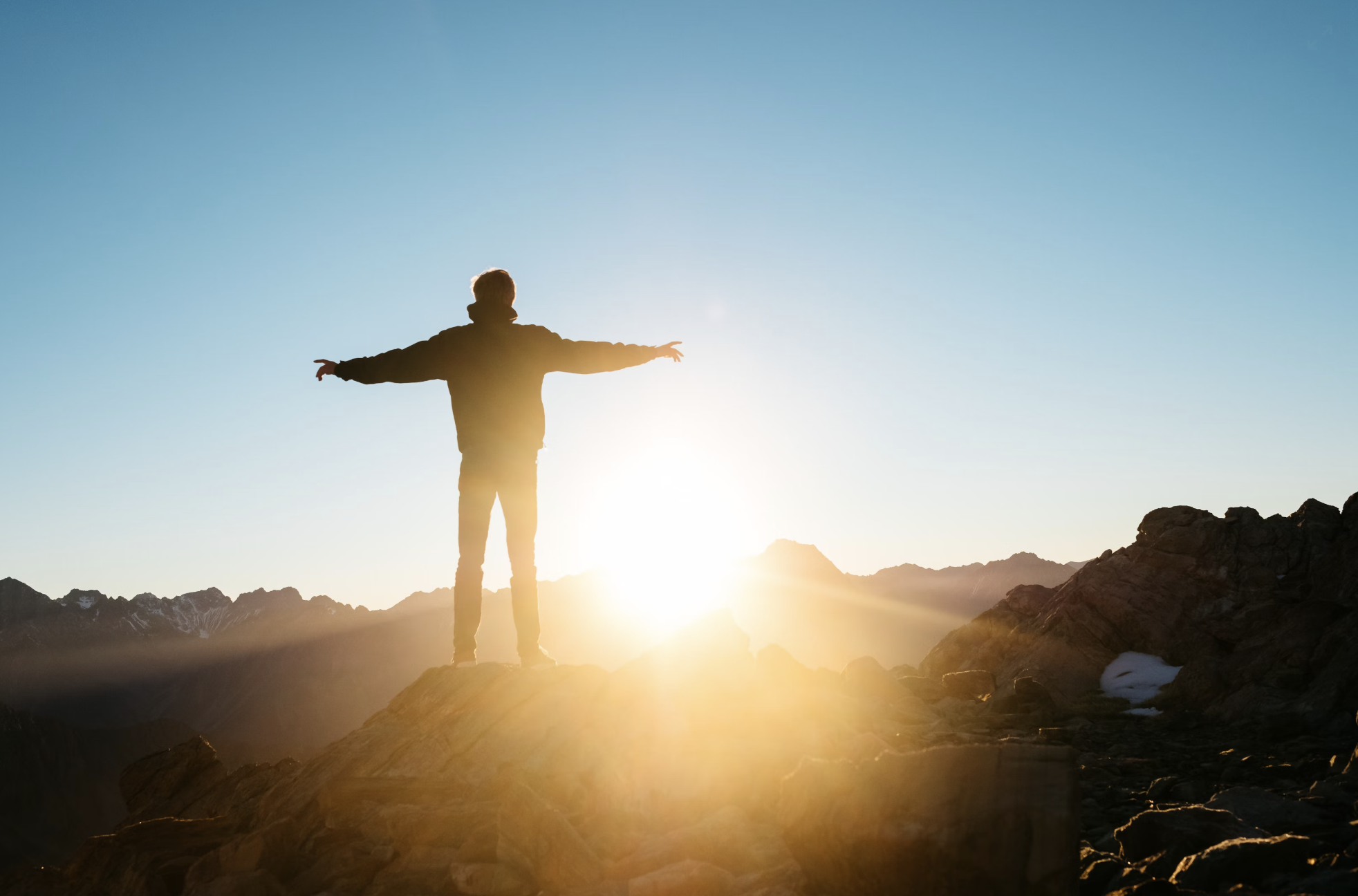 Man standing on top of mountain with arms wide enjoying awesome sunrise