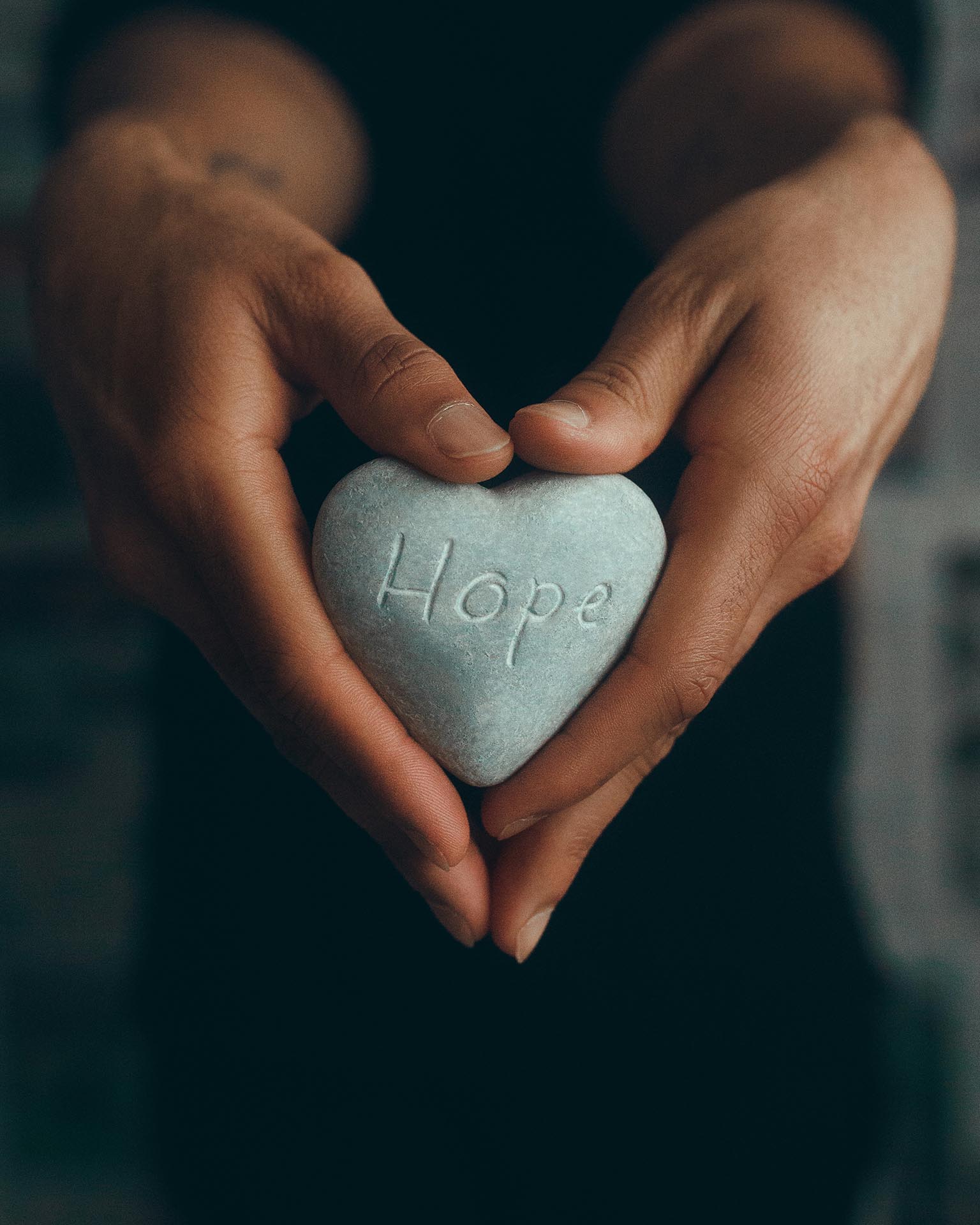 Hands holding on a heart shaped stone that have 'Hope' written on it